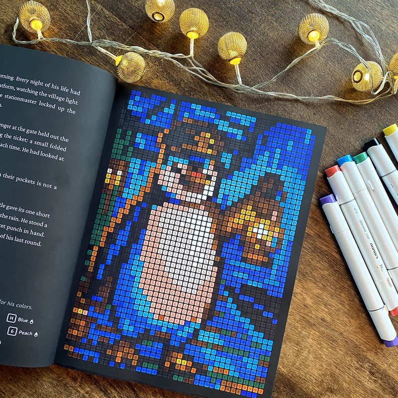 The advent calendar book open on the finished first portrait, the penguin conductor with his lantern, markers and fairy lights around it.